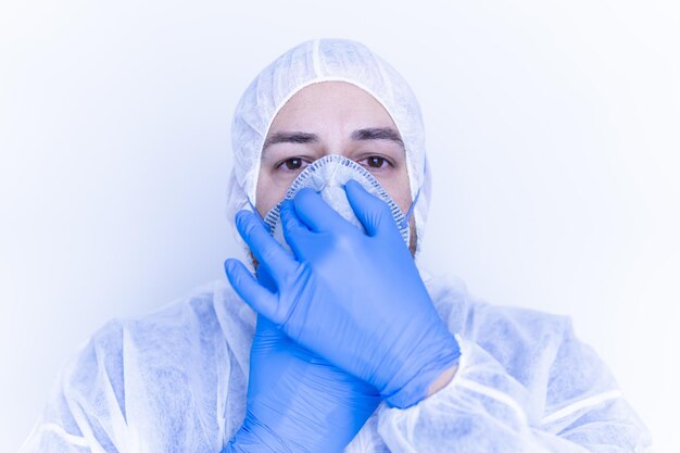 Trabalhador médico em um terno de plástico colocando uma máscara facial com luvas de plástico azuis