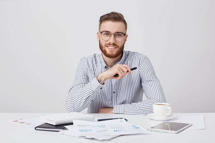 Foto grátis trabalhador profissional do sexo masculino com barba espessa e penteado moderno, usa óculos redondos e camisa formal