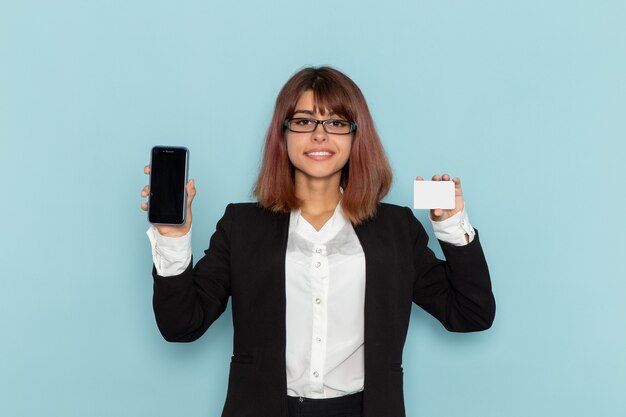 Trabalhadora de escritório feminina de terno estrito segurando um cartão e um telefone na superfície azul.