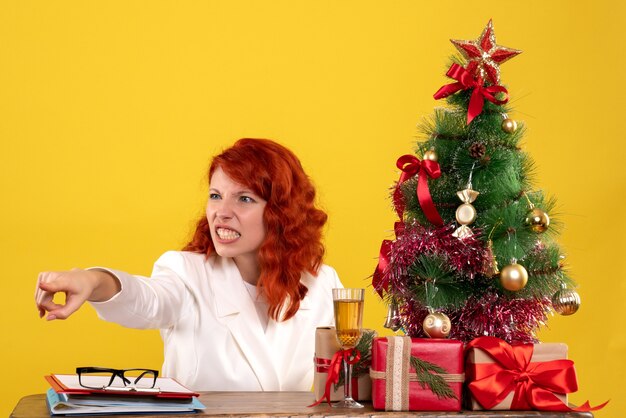 trabalhadora sentada atrás da mesa com presentes de Natal e árvore em amarelo