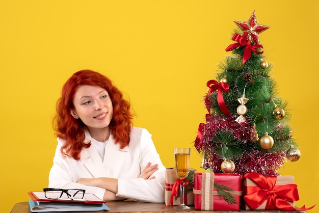 Trabalhadora sentada atrás da mesa com presentes de natal e árvore em amarelo