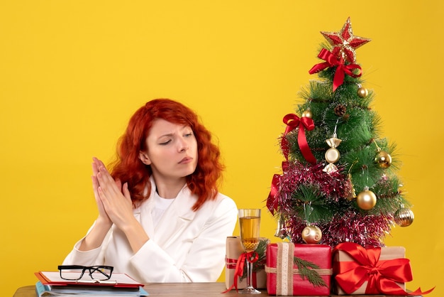 trabalhadora sentada atrás da mesa com presentes de Natal e árvore em amarelo