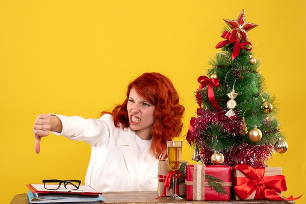 trabalhadora sentada atrás da mesa com presentes de Natal e árvore em amarelo