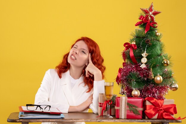 trabalhadora sentada atrás de sua mesa com a pequena árvore de natal e presentes em amarelo