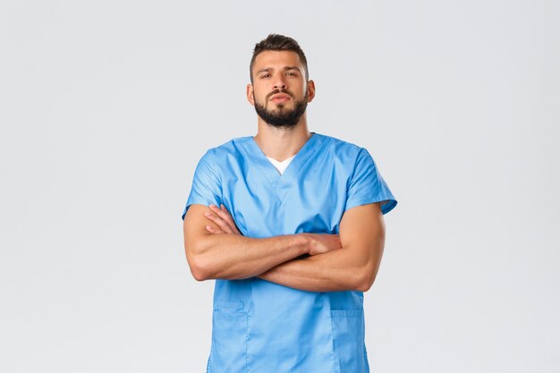 Trabalhadores da saúde, medicina, covid-19, conceito de auto-quarentena pandêmica. Médico hispânico, forte e confiante, de aparência séria, enfermeiro de uniforme azul, peito de mãos cruzadas, autoconfiante, salvar pacientes.