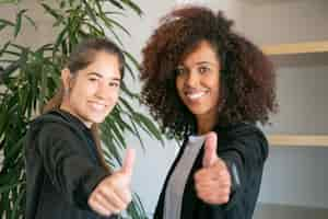 Foto grátis trabalhadores de escritório femininos felizes manuseando e sorrindo. duas alegres empresárias profissionais juntas e posando na sala de reuniões. conceito de trabalho em equipe, negócios, sucesso e cooperação