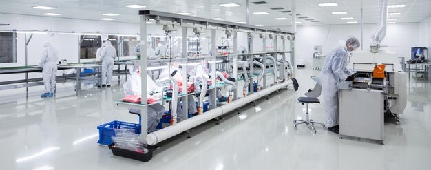 Trabalhadores de fábrica em trajes de laboratório brancos e luvas de látex pretas trabalhando com alguns equipamentos modernos em uma imagem panorâmica de sala muito limpa