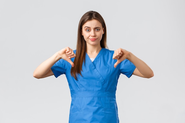 Trabalhadores de saúde, previnem o conceito de vírus, seguro e medicina. Enfermeira ou médico cético e chateado com uniforme azul, sorriso de decepção, mostrando o polegar para baixo, não gosta de algo