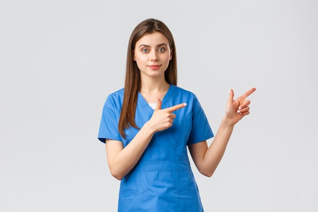 Trabalhadores de saúde, previnem o conceito de vírus, seguro e medicina. Jovem enfermeira ou médico de uniforme azul apontando o dedo para a direita, recomendar banner ou promoção para pacientes da clínica