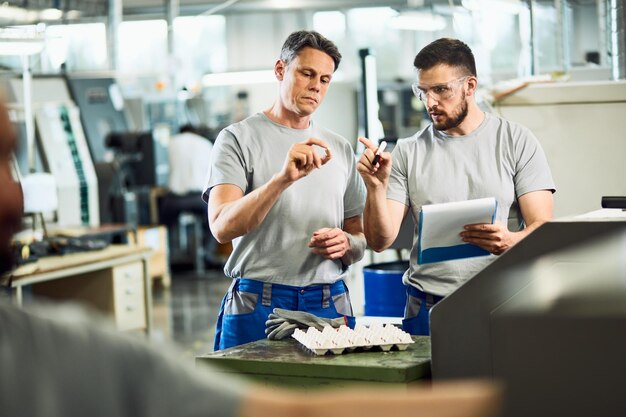 Trabalhadores industriais cooperando ao fazer o controle de qualidade de produtos manufaturados em uma fábrica