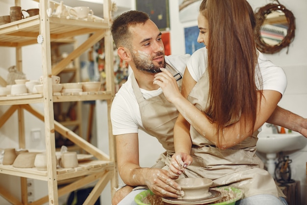 Trabalho criativo mútuo. Jovem casal lindo em roupas casuais e aventais. Pessoas criando uma tigela em uma roda de oleiro em um estúdio de argila.