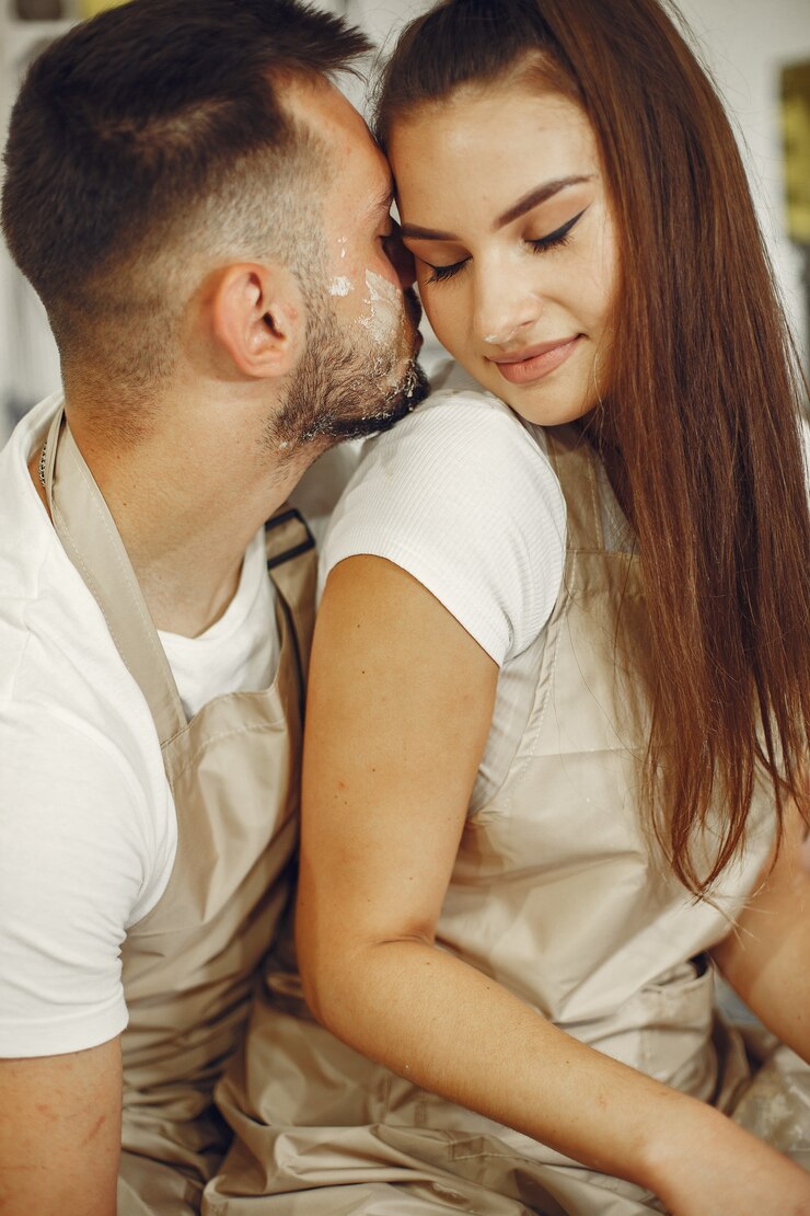 Foto grátis trabalho criativo mútuo. jovem casal lindo em roupas casuais e aventais. pessoas criando uma tigela em uma roda de oleiro em um estúdio de argila.