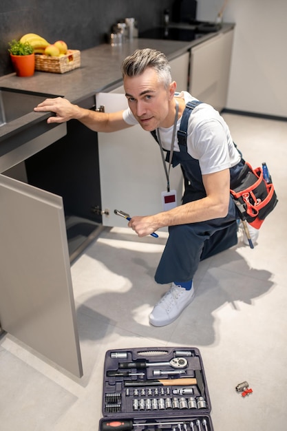 Foto grátis trabalho doméstico vista superior do homem de macacão com distintivo agachado perto da pia