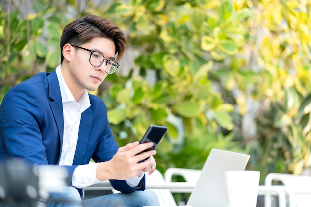 Traje formal de empresário inteligente sente-se relaxe mão segure smartphone com laptop trabalhando televideoconferência reunião trabalho remoto social distanceasian ale trabalhando relaxe no fundo do jardim parque