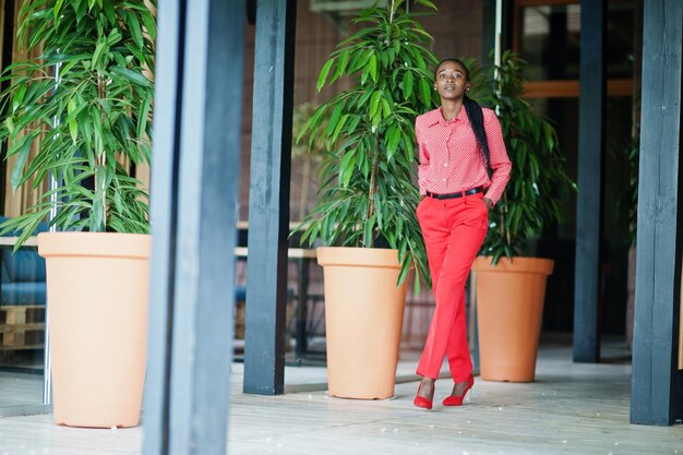 Tranças bonitas, negócios, senhora afro-americana, pessoa brilhante, mandona, amigável, usa camisa vermelha e calças de escritório