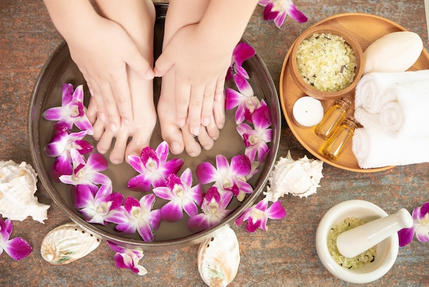 Tratamento e produto spa para pés e mãos femininas. flores da orquídea em uma tigela de cerâmica.