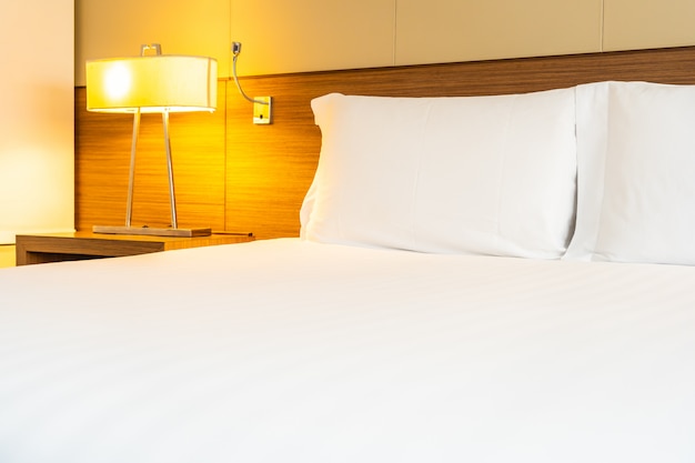 Travesseiro branco confortável e cobertor na cama com lâmpada de luz Foto gratuita