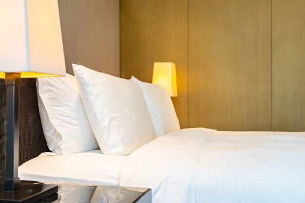 Travesseiro branco confortável e cobertor na cama com lâmpada de luz