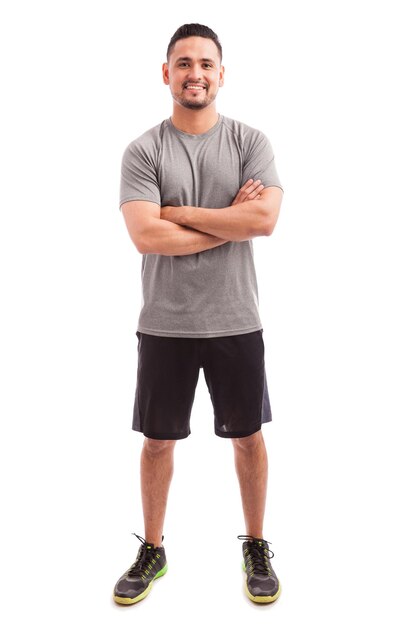Treinador de fitness masculino hispânico com os braços cruzados e sorrindo em um fundo branco