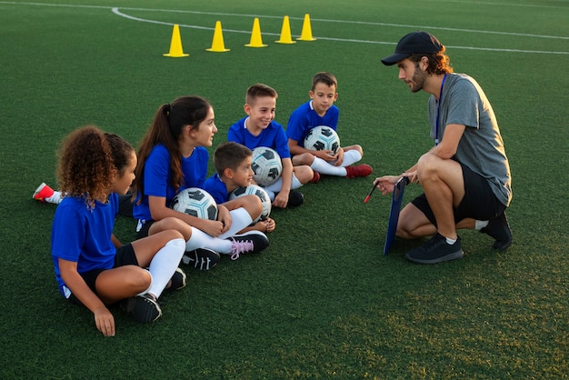 Foto grátis treinador de futebol ensinando vista lateral para crianças