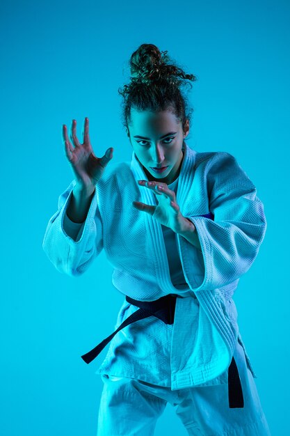Treinamento ativo. Judô feminino profissional no quimono de judô branco praticando e treinando isolado no fundo do estúdio azul neon.