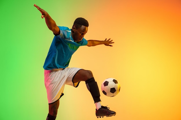 Treinamento de jogador de futebol de futebol masculino afro-americano imparável em ação isolado em fundo de estúdio gradiente em luz de neon Conceito de estilo de vida saudável de realizações de ação de movimento