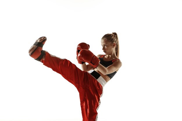 Treinamento de lutador de kickboxing feminino jovem isolado na parede branca. menina loira caucasiana em sportswear vermelho praticando artes marciais. conceito de esporte, estilo de vida saudável, movimento, ação, juventude.