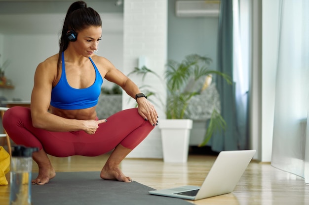 Treinamento pessoal feminino usando laptop enquanto realiza aula on-line em casa
