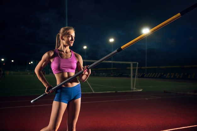 Treinamento profissional de salto com vara feminino no estádio à noite. praticar ao ar livre.