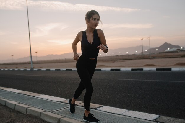 Treinamento, rodando na estrada na manhã ensolarada de mulher bonita. Verão, forte desportista, energia, motivação, estilo de vida saudável, treino, felicidade, desfrutar do desporto