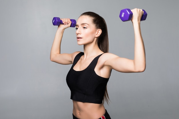 Treino de mulher sorridente fitness com halteres pequenos isolados em uma parede branca