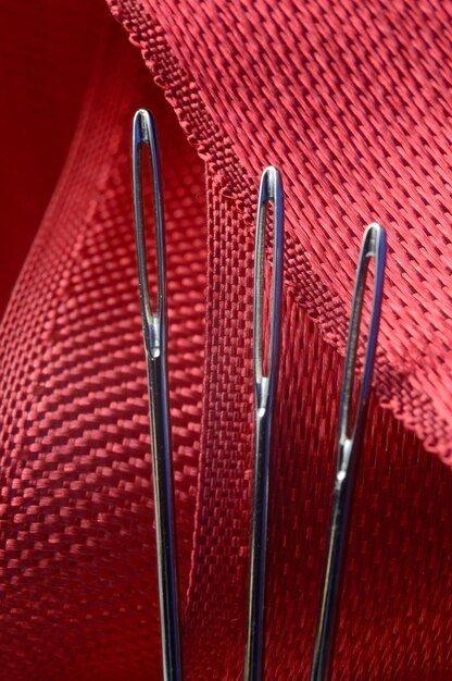 Três agulhas de costura em um fundo de tecido vermelho. fechar-se. Foto Premium