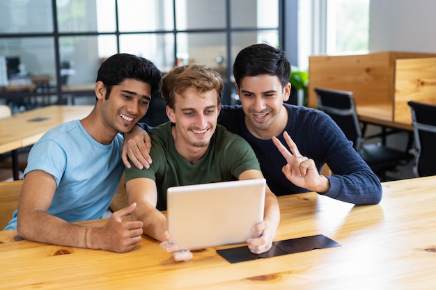 Três alunos felizes, abraçando e tendo chamada de vídeo no tablet