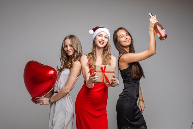 Três amigas alegres em lindos vestidos celebram o natal
