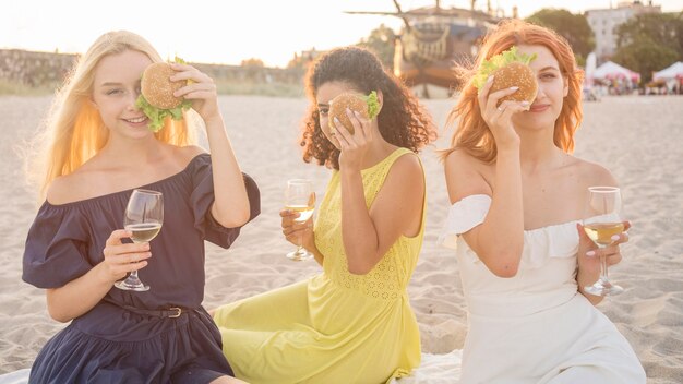 Três amigas degustando hambúrgueres na praia