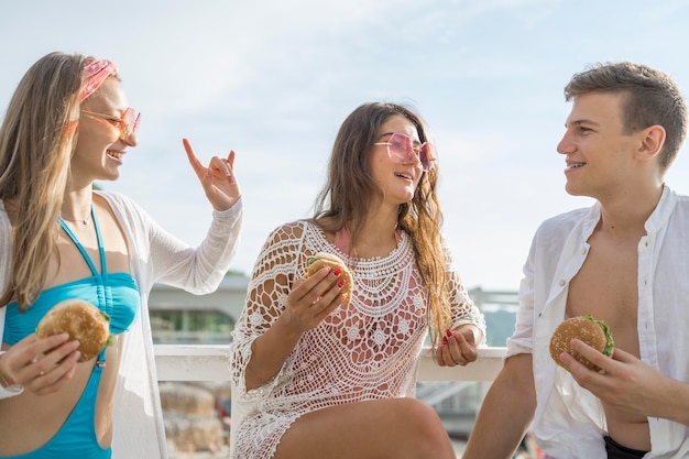 Três amigos comendo hambúrgueres juntos na praia