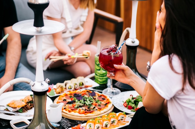 Três amigos jantando com salada de pizza de sushi e cachimbo de água