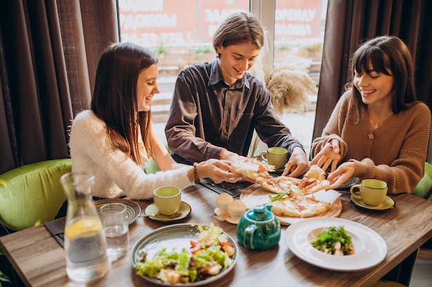 Três amigos juntos comendo pizza em um café