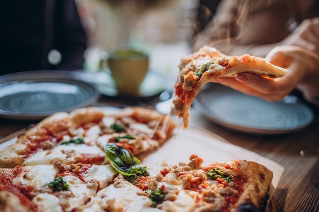 Três amigos juntos comendo pizza em um café