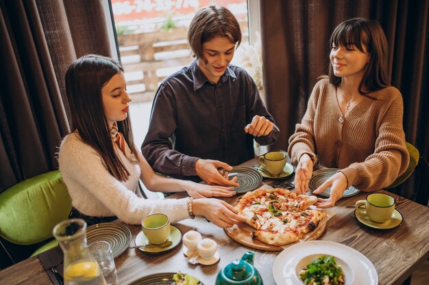 Três amigos juntos comendo pizza em um café