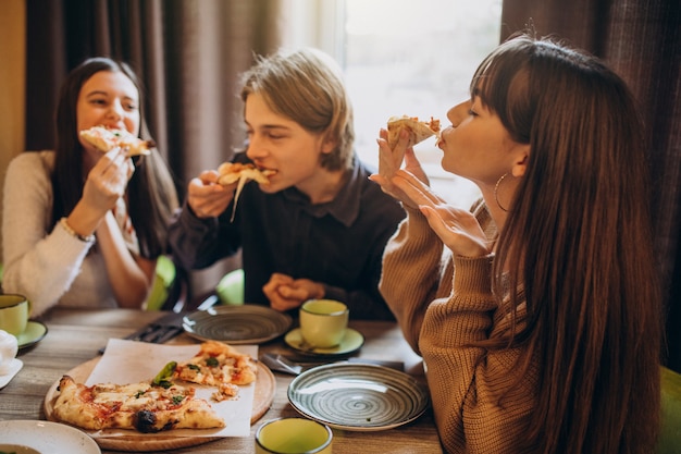 Três amigos juntos comendo pizza em um café