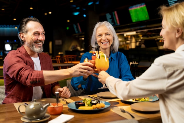 Três amigos seniores conversando em um restaurante enquanto torcendo com bebidas