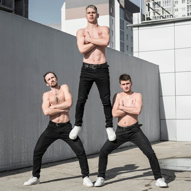 Três artistas de hip hop sem camisa posando juntos