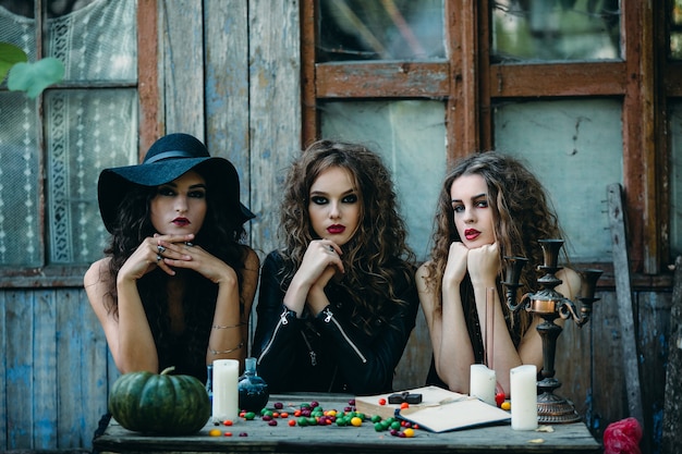 Três bruxas estão sentadas em uma mesa na véspera do halloween