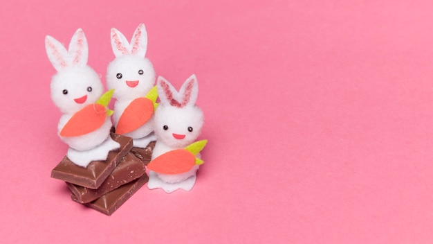 Três coelhos brancos com cenoura em pedaços de chocolate sobre o fundo rosa