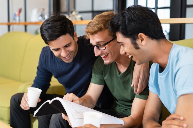 Três colegas estudantes lendo livros didáticos, rindo e bebendo