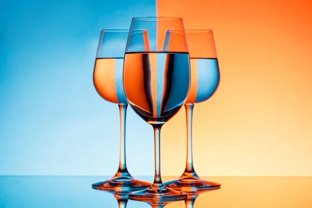 Três copos de vinho com água sobre o fundo azul e laranja.