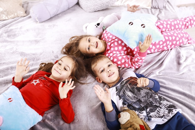 Três crianças felizes estão deitadas no cobertor vestido com roupa de noite
