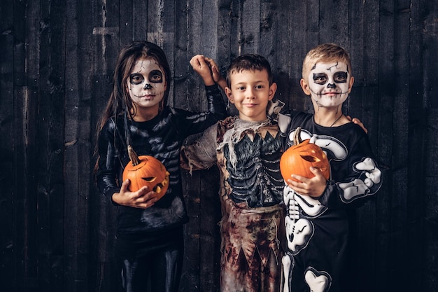 Três crianças multirraciais em trajes assustadores posando com abóboras em uma casa velha. Conceito de dia das bruxas.