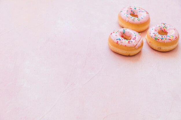 Três deliciosos donuts com granulado no fundo rosa